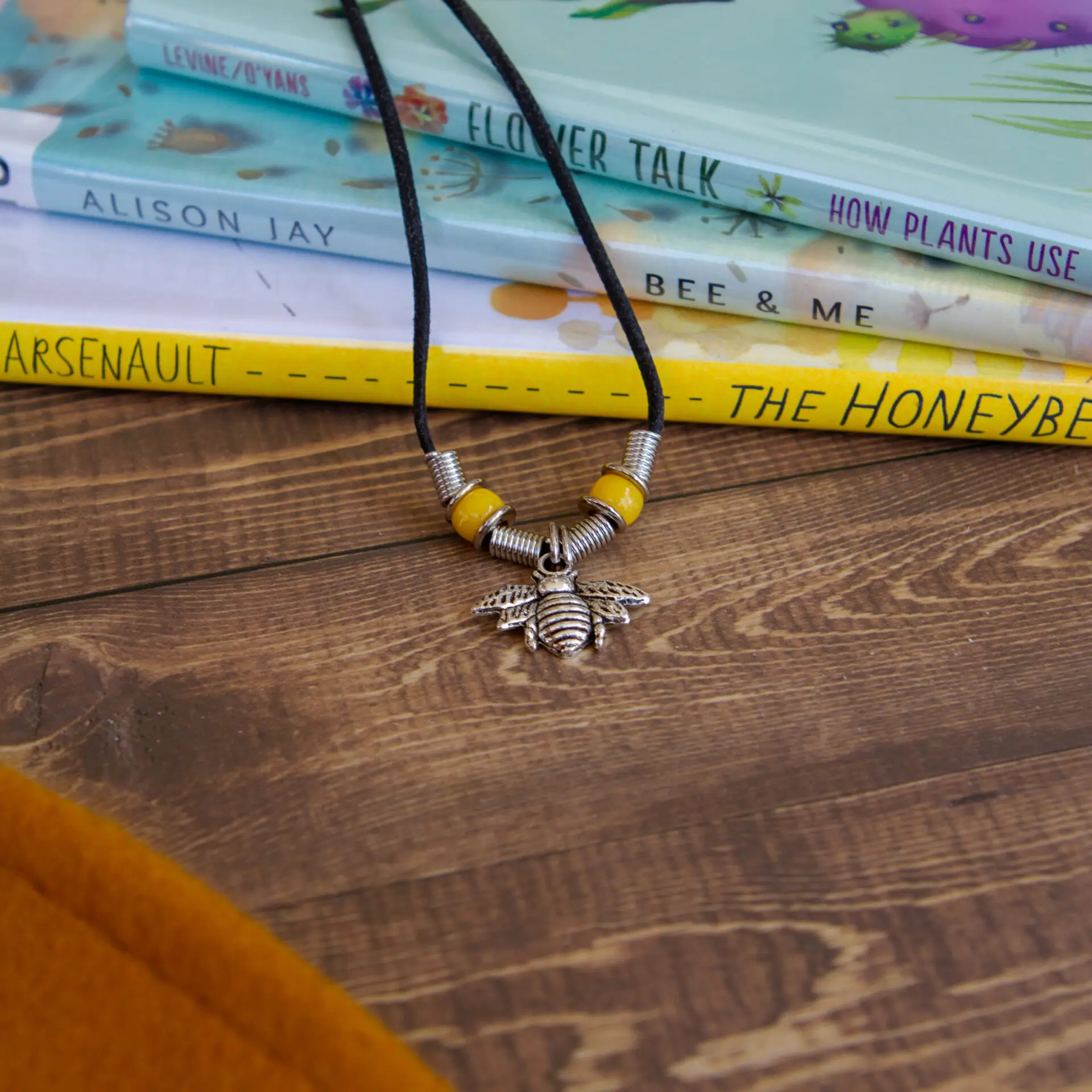 A necklace with a sun pendant lies on a wooden surface near books.
